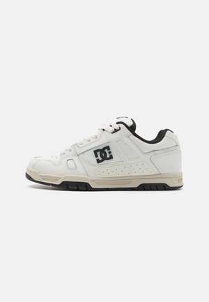 Baskets basses blanches avec logo DC noir sur le côté, semelle beige, fermeture à lacets et doublure intérieure noire, vues de profil.