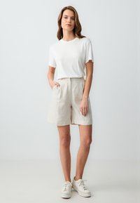 T-shirt blanc à manches courtes associé à un short en lin beige, présentant une coupe décontractée et des poches latérales, stylisé avec des baskets légères.