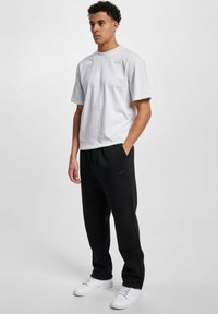 Hvit bomulls t-skjorte med korte ermer og brystlomme, kombinert med svarte fleece-joggebukser og hvite joggesko, med sidelommer.