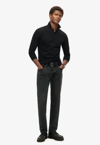 Polo negro de manga larga con cuello, combinado con jeans gris oscuro y zapatos negros. Presenta un diseño ajustado y acentos minimalistas.