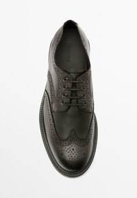 Schwarze Lederschuhe mit Flügelspitze, durchbrochenen Details, sechs Ösen und einer runden Zehenpartie mit strukturierter Sohle.