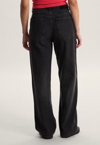 Černé džíny s širokými nohavicemi a vysokým pasem, s dvěma náprsnými kapsami na zádech a neupraveným lemem. Vyrobené z denimu s mírně strukturovaným povrchem.