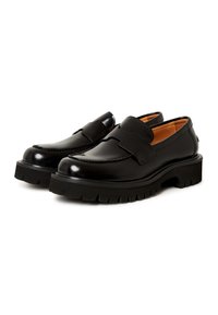 Zwarte leren loafers met een gladde afwerking, voorzien van een brede band over de bovenkant, een dikke zwarte rubberen zool en gestikte details.