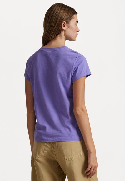 Maglietta viola a maniche corte in cotone, con scollatura rotonda e vestibilità comoda, abbinata a pantaloni beige. Vista posteriore mostrata.