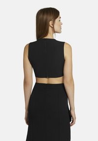 Zwarte cropped top met een hoge halslijn en mouwloos ontwerp, voorzien van een ritssluiting aan de achterkant. Soepele textuur, strakke pasvorm tegen een effen achtergrond.