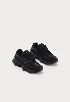 Paire de baskets de sport noires avec semelles épaisses et design à lacets sur un fond clair uni.