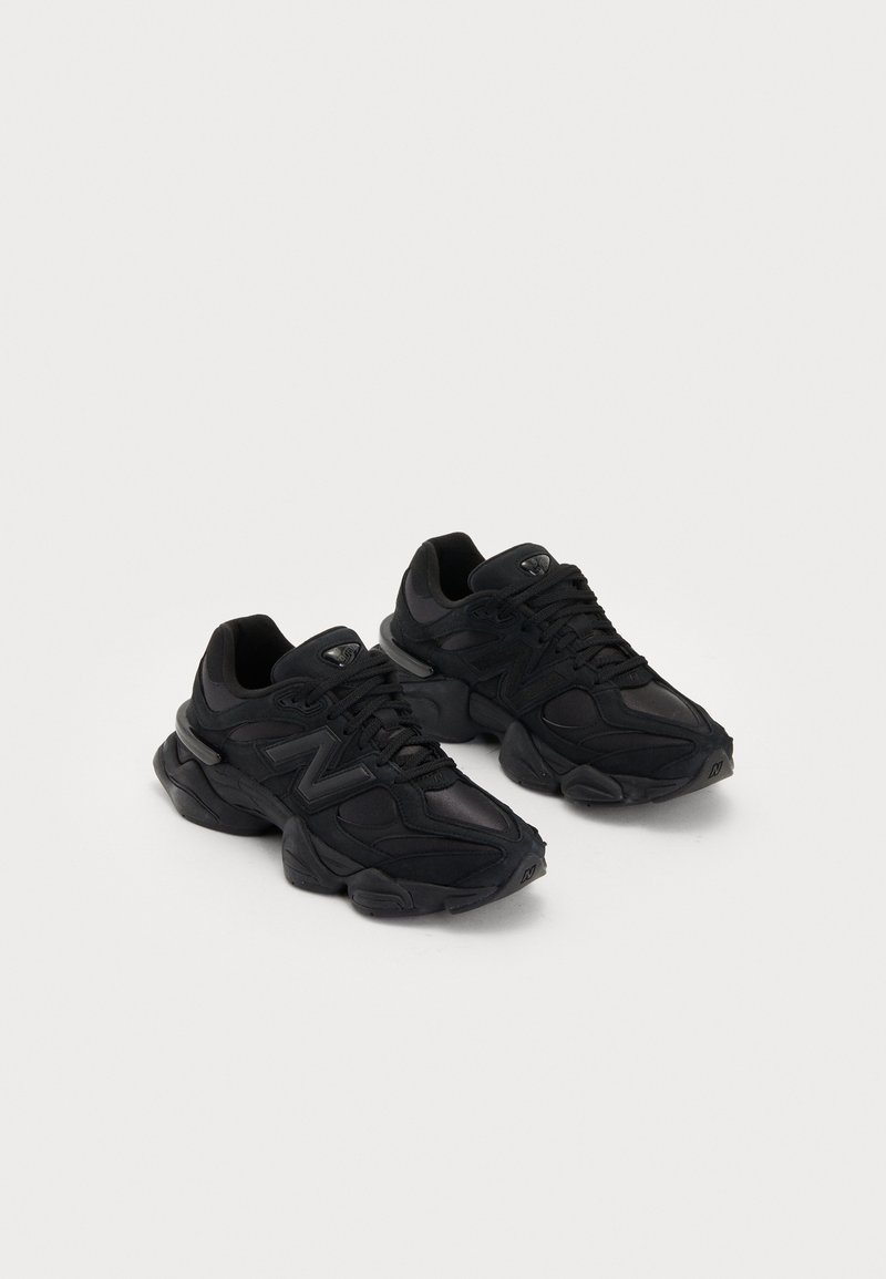 Paire de baskets de sport noires avec semelles épaisses et design à lacets sur un fond clair uni.