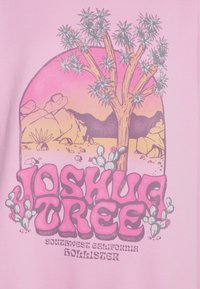Rosa tyg med en grafisk design av ett Joshua-träd, berg och kaktusar. Tydlig text "Joshua Tree" längst ner med en bakgrund av solnedgång.