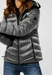 Grå vadderad jacka med huva, utrustad med kviltad design, zip-front och fickor, samt en slät, glänsande yta. Accenterad med svarts hårdvara.