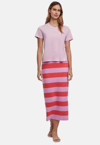 Top rosa chiaro a maniche corte abbinato a una gonna lunga a strisce rosa e rosse. La gonna presenta strisce orizzontali ampie alternate. Sono inclusi sandali.