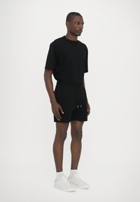 Sort jersey t-shirt med korte ærmer, parret med sorte shorts med snøre. Hvide sneakers og sokker fuldender outfittet. Glat tekstur.