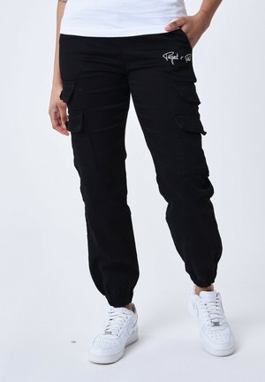 Pantalons cargo noirs avec des poignets élastiques et plusieurs poches latérales. Présente un petit logo brodé sur la hanche. Fabriqué en tissu durable.