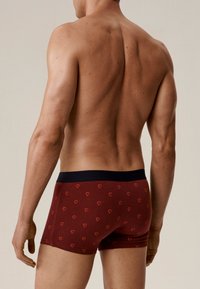 Czerwone bokserki z małymi wzorami czerwonych serc, z granatowym paskiem w talii; materiał wydaje się miękki, o dopasowanym kroju.