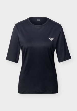 T-shirt noire à manches courtes et col rond avec un petit logo blanc sur le côté gauche de la poitrine, sur un fond gris clair uni.