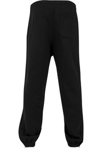 Svarta sweatpants gjorda av ett mjukt tyg. Har elastisk midja, avsmalnande ben och en enda bakficka. Ribbad mudd vid anklarna.