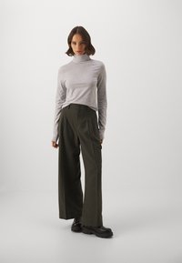Hallide hallise käisekontuuriga turtleneck, mis on paaritatud oliivroheliste laia säärega pükstega, millel on kõrge vöökoht ja nööpide detail. Mustad tursked saapad.