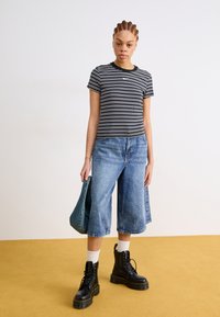 Μαύρο και άσπρο ριγέ κοντομάνικο μπλουζάκι, μπλε φαρδιά τζιν σορτς, μαύρες μποτες με δέσιμο, με μια επιπλέον μπλε τζιν τσάντα στο χέρι.