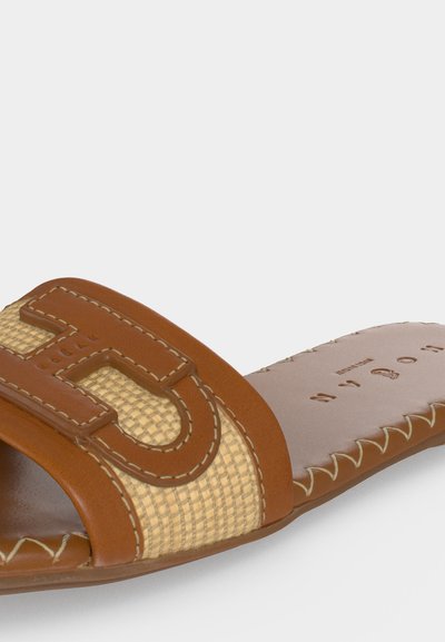 Καφέ δερμάτινο σανδάλι slide με πλεγμένη μπεζ λεπτομέρεια και μεγάλο ραμμένο γράμμα "B" στο λουράκι, με ορατά υφασμένα άκρα σόλας.