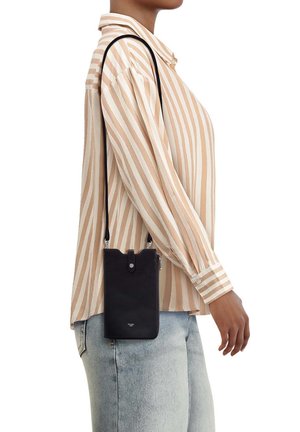 Persona che indossa una camicia a righe beige e bianca e jeans azzurri chiari, con una piccola borsa nera a tracolla sulla spalla.