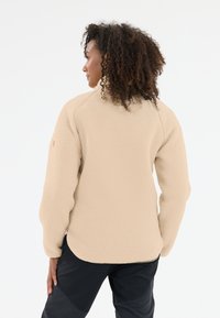 Beige fleecejakke med en tekstureret overflade, høj krave og raglanærmer. Har en rund søm og minimal dekoration.