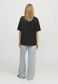 Černé oversize tričko s krátkým rukávem, doplněné o světle modré volné džíny. Materiál je měkký s hladkou texturou. Jednoduchý design, bez vzorů.