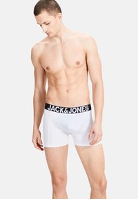 White boxer shorts with a black waistband, featuring the brand name "JACK & JONES" in bold white letters. Smooth fabric, close-fit design.
