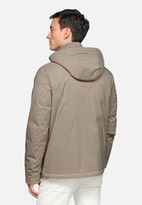 Giacca a vento beige con cappuccio, dalla consistenza liscia e dal taglio morbido. Presenta un design semplice senza loghi o motivi visibili.