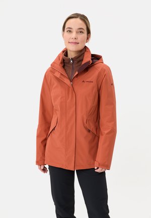 Waterdichte oranje jas met een capuchon, rits aan de voorkant, zijzakken en logo-detaillering, gecombineerd met een bruine binnenlaag en zwarte broek.