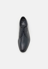Chaussure noire en cuir à lacets avec une surface texturée, dotée d'un bout arrondi et d'une étiquette de confort à l'intérieur en texte blanc.