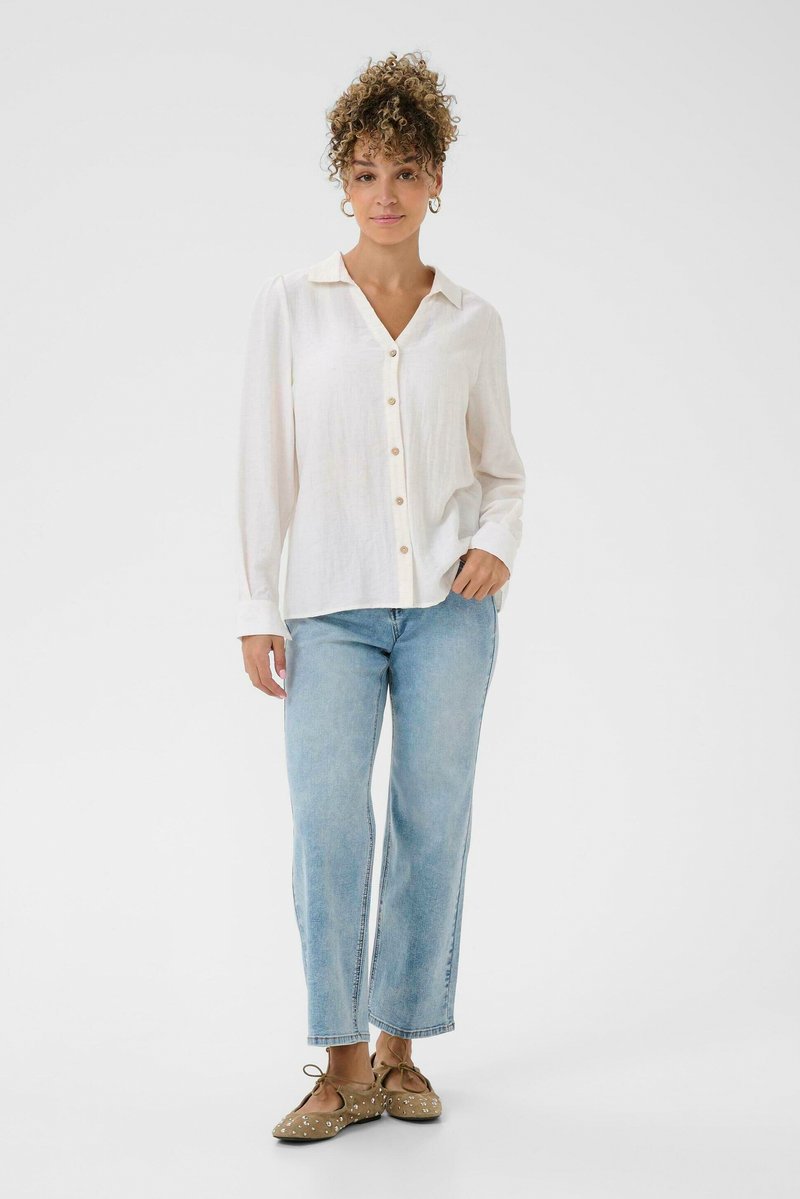 Chemise blanche à manches longues avec un col, associée à un jean droit bleu clair et des ballerines beige avec des ornements.
