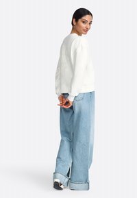 Felpa color crema con maniche lunghe, polsini a coste e motivo floreale sulla schiena, abbinata a pantaloni in denim larghi di colore blu chiaro.
