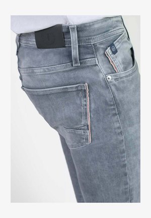 Grijze denim jeans met een licht vervaagde uitstraling, voorzien van een achterzak met een rood-witte gestikte accent en een zwarte taillebandlabel.