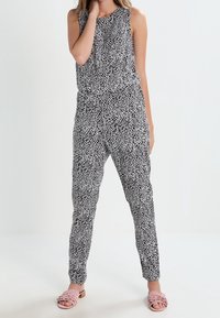Czarny i biały kombinezon w wzory z bezrękawowym fasonem i zwężanymi nogawkami. Wykonany z lekkiego materiału, z elastycznym pasem.