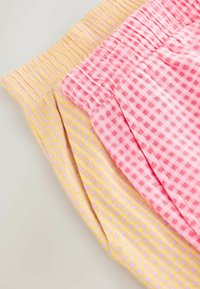 Deux paires de shorts à taille élastique en tissu vichy jaune et rose, pliées et superposées sur un fond neutre.
