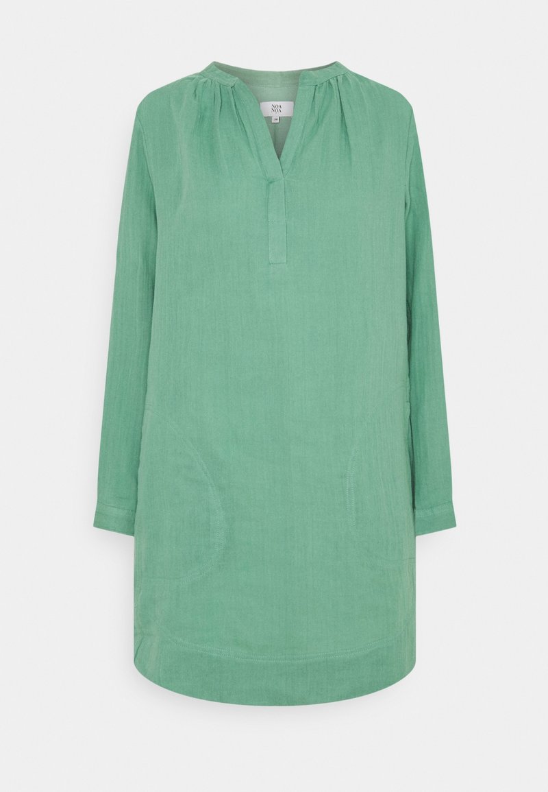 Tunique en lin vert avec un col en V, manches longues et poches latérales. Présente une finition texturée et un ourlet légèrement incurvé.