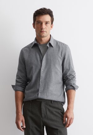 Grijs geruit overhemd met kraag, met lange mouwen opgerold, gedragen over een grijs ronde hals t-shirt, gecombineerd met donker getextureerde broeken.