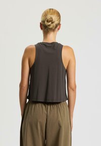 Dunkelgraues, kurzes Tanktop mit Rundhalsausschnitt und ärmellosem Design, kombiniert mit lockeren khakifarbigen Hosen. Glatte Textur, minimale Details.