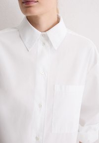 Witte katoenen shirt met een klassieke kraag, knoopsluiting, één borstzak en opgerolde mouwen. Gladde textuur, casual pasvorm.