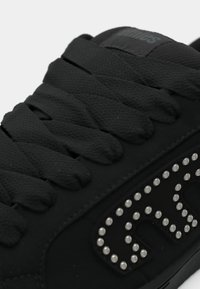 Μαύρο αθλητικό παπούτσι με υφασμάτινη επιφάνεια με υφή, στρογγυλά κορδόνια και διακοσμητικό μοτίβο από ασημένιες ακτίνες στο πλάι.