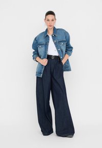 Giacca di jeans oversize in blu chiaro, abbinata a jeans a vita alta blu scuro a gamba larga e a una maglietta bianca. Cintura nera con dettaglio in fibbia argentata.