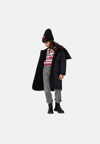 Manteau long matelassé noir avec capuche, sweat-shirt rayé gris, jean gris et bottes noires. L'enfant porte un bonnet noir avec une touche de rouge.