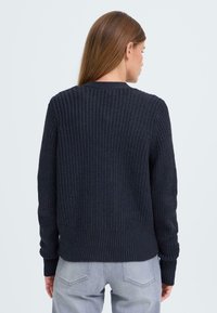Pull en maille bleu marine foncé avec un design à côtes, un col rond et des manches longues. Présente un tissu texturé et un ourlet ajusté.