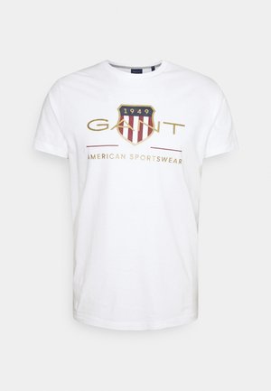 Weißes T-Shirt mit Rundhalsausschnitt, mit einem Schildemblem, der Aufschrift "1949" und "GANT American Sportswear" in Gold und Rot auf der Brust bedruckt.