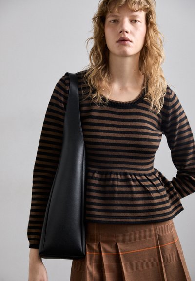 Barna és fekete csíkos kötött pulóver peplum alsó résszel, kockás barna szoknyával párosítva. Egy fekete bőr válltáska van nála.