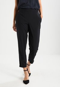 Černé, lehké, zúžené kalhoty s hladkým povrchem a bočními kapsami. Nosené s vzorovaným topem a černými lodičkami na kotníkovém řemínku.