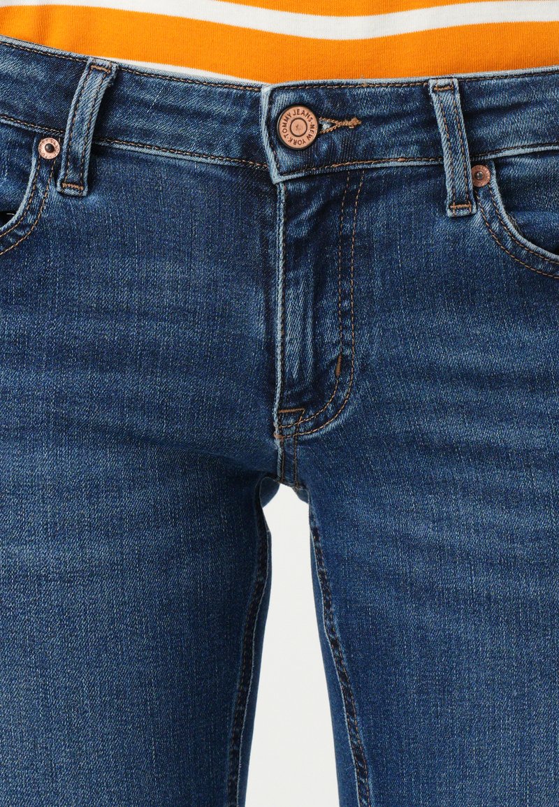 Granatowe dżinsy o slim fit, z mosiężnym wykończeniem, z przeszytymi kieszeniami i zapięciem na guzik w pasie.