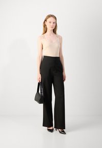 Beige tank top with chain strap accents, black high-waisted wide-leg trousers, black pointed-toe heels, and small black handbag.