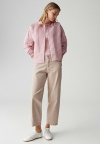 Różowo-biała koszula w paski na guziki, beżowe spodnie i białe trampki. Koszula ma luźny krój i bufiaste rękawy.