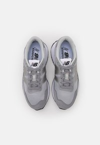 Zapatillas deportivas grises elaboradas con materiales de malla y ante, que cuentan con un collar acolchado, cordones y un logotipo en la lengüeta y el costado.