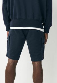 Marinefarbene Cargo-Shorts aus Baumwolle mit glatter Textur, ausgestattet mit Seitentaschen und einem knielangen Schnitt. Strapazierfähige Nähte und bequemer Sitz.